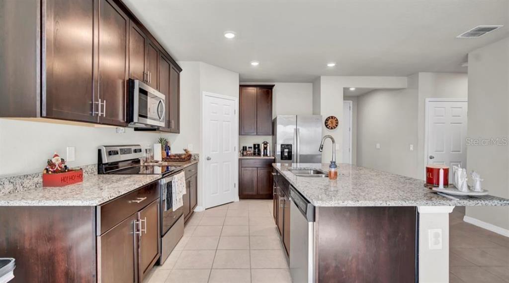 A kitchen features dark wood cabinetry, granite countertops, a center island, and stainless steel appliances — 3041 CASSIDY LANE, HAINES CITY, FL