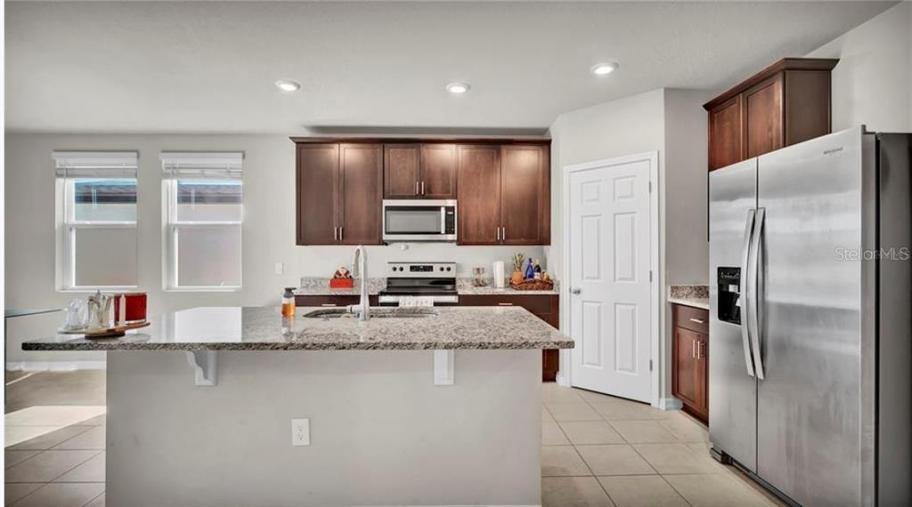 A kitchen features dark wood cabinets, granite countertops, a center island, and stainless steel appliances — 3041 CASSIDY LANE, HAINES CITY, FL