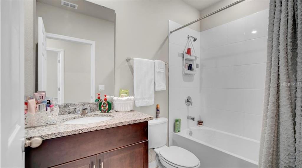 A bathroom features a dark wood vanity with a granite countertop, toilet, and shower-tub combo — 3041 CASSIDY LANE, HAINES CITY, FL