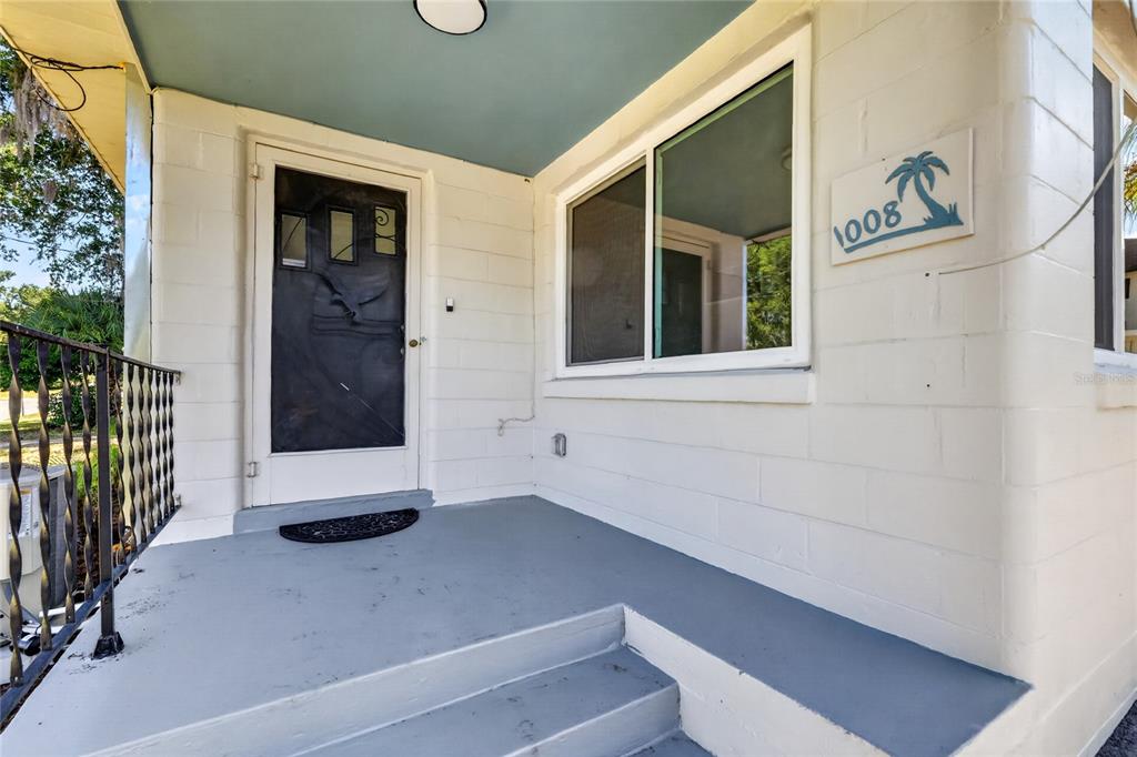 A front porch with a gray concrete floor, a white door, and a palm tree sign — 1012 N BAKER STREET, MOUNT DORA, FL