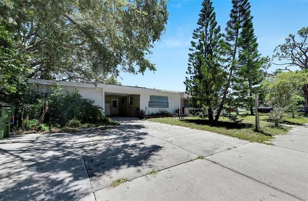 A single-story house with a concrete driveway, a carport, and tall pine trees in front — 2695 S EAST AVENUE, SARASOTA, FL