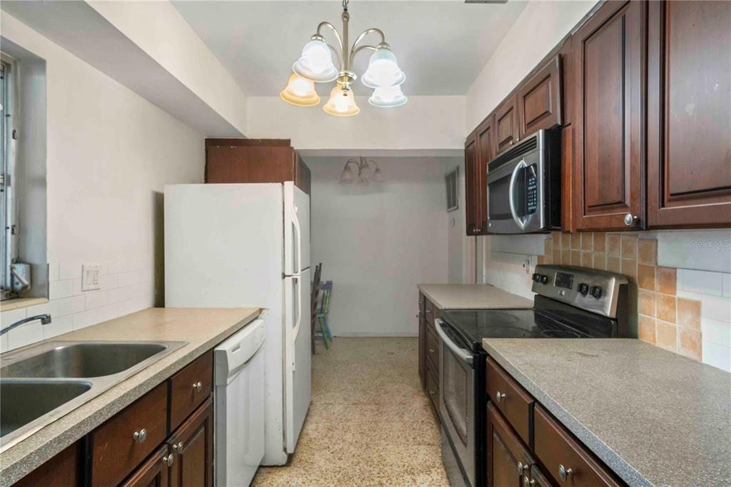 A galley kitchen features dark wood cabinets, laminate countertops, and white appliances — 2695 S EAST AVENUE, SARASOTA, FL