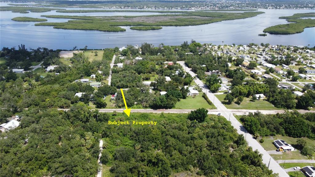 An aerial view shows a wooded, undeveloped lot marked by a yellow arrow near water — 27520 MITCHELL AVENUE, PUNTA GORDA, FL