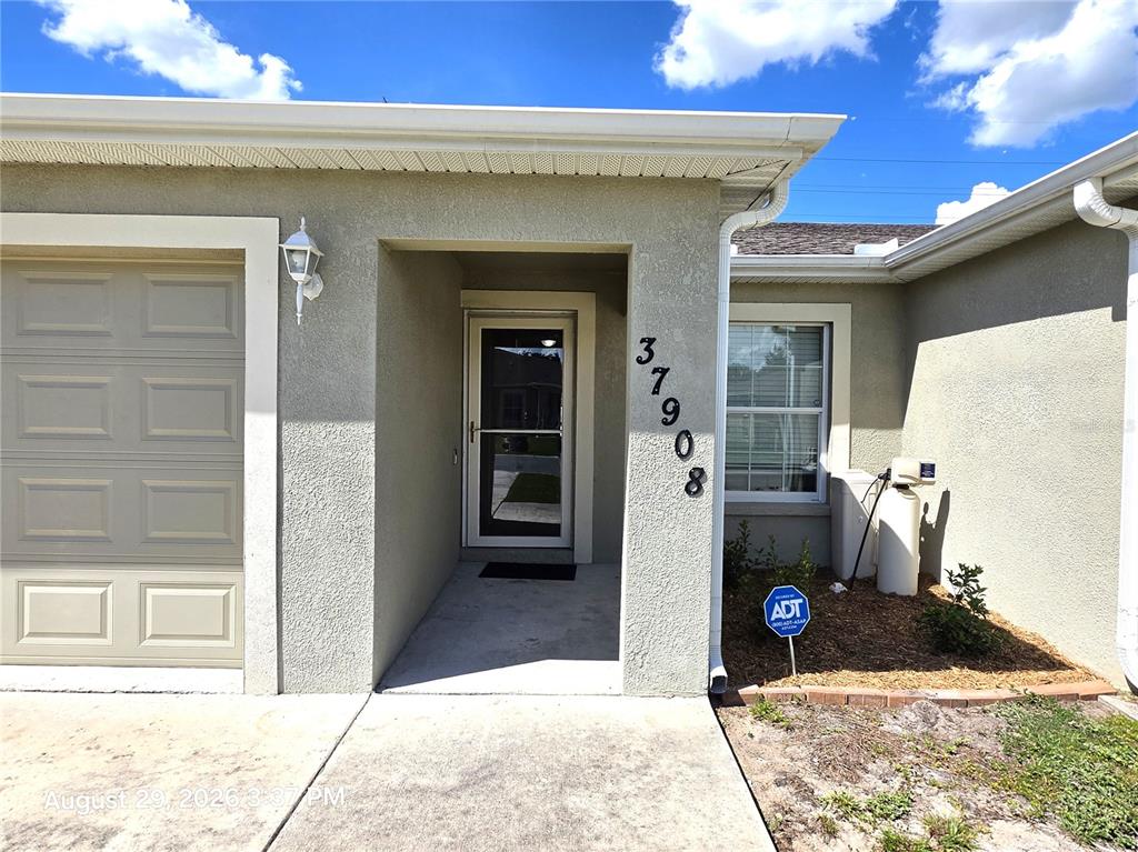 The exterior of a single-story house features a front entrance, a garage, and house numbers — 37908 PRAIRIE ROSE LOOP, ZEPHYRHILLS, FL