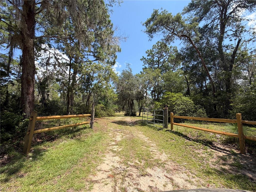 A dirt path leads through a wooden fence and metal gate into a wooded area — 24605 and 24645 NE 177TH TERRACE, FORT MC COY, FL