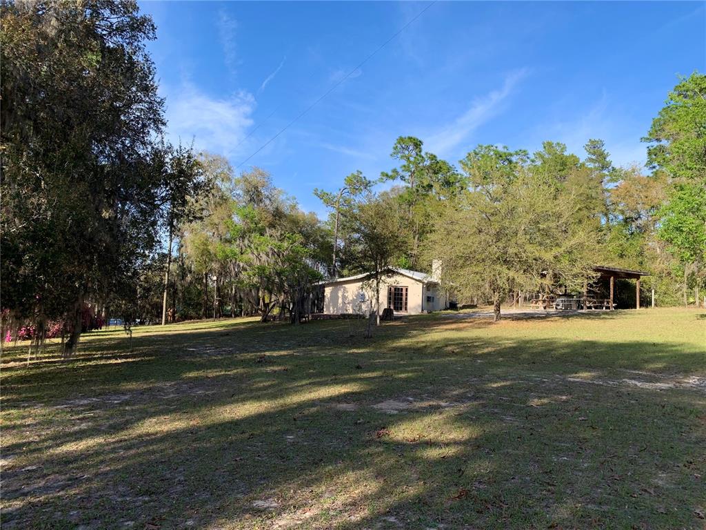 A single-story house sits on a large, grassy lot surrounded by mature trees — 24605 and 24645 NE 177TH TERRACE, FORT MC COY, FL