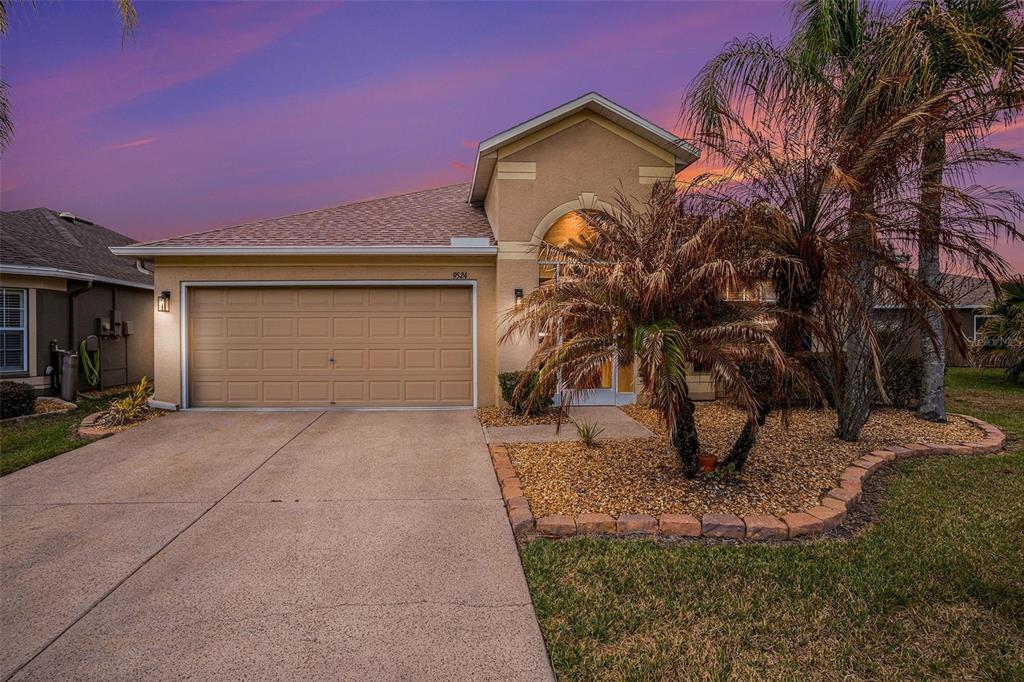 A single-story suburban house with a tan stucco exterior, a two-car garage, and palm trees — 9524 ROLLING CIRCLE, SAN ANTONIO, FL