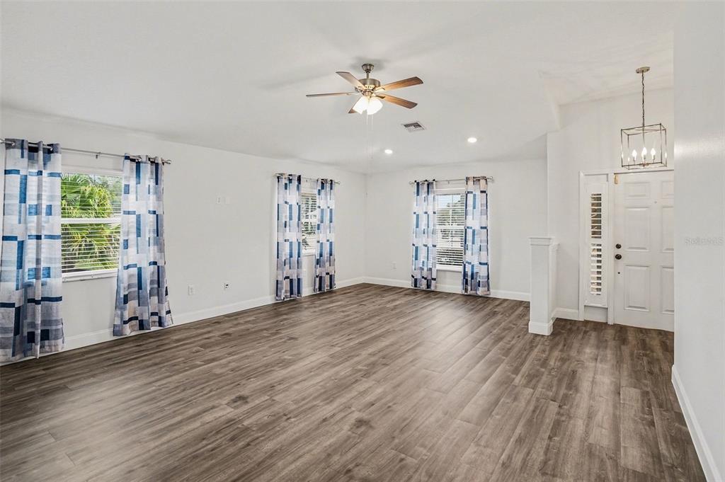 An empty living room features wood-look flooring, white walls, a ceiling fan, and blue curtains — 9524 ROLLING CIRCLE, SAN ANTONIO, FL