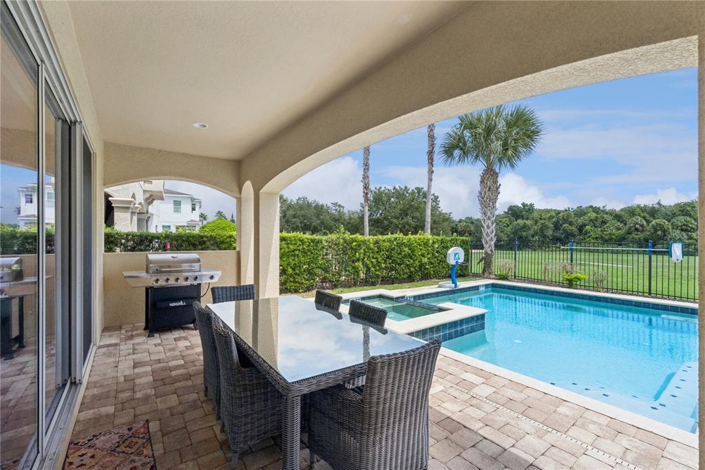A covered patio features a dining set, a grill, and a pool with an attached spa — 785 DESERT MOUNTAIN COURT, KISSIMMEE, FL