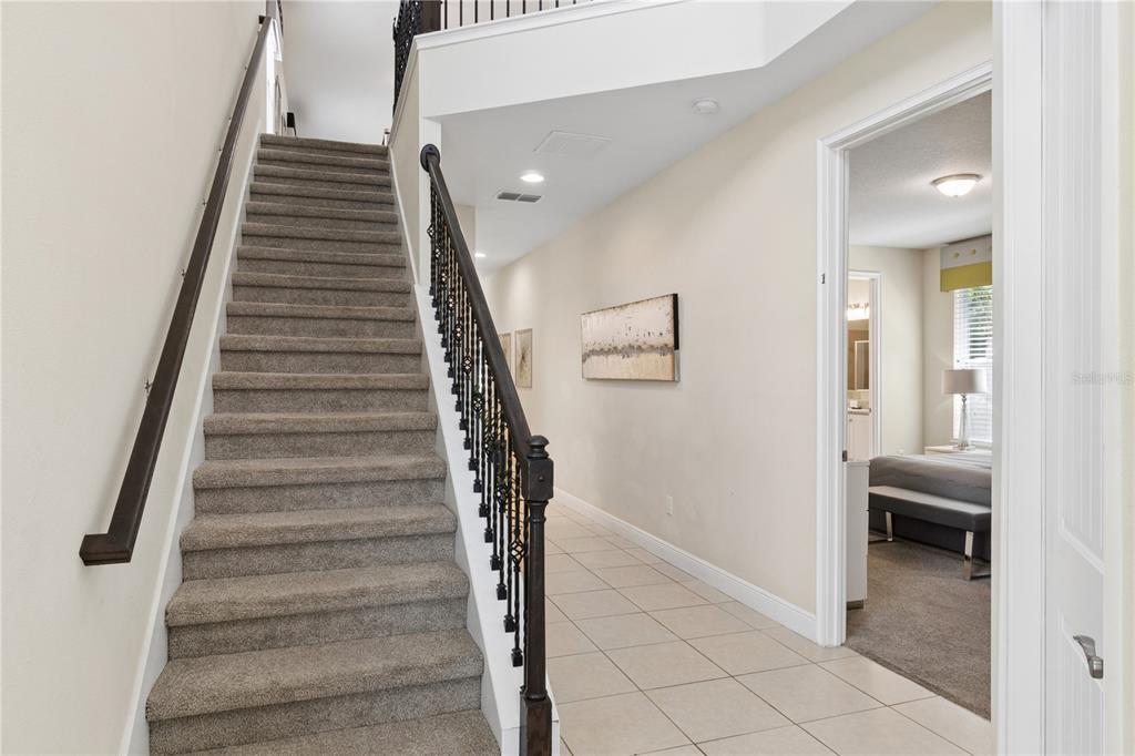 A carpeted staircase with a dark metal railing sits beside a tiled hallway and bedroom — 785 DESERT MOUNTAIN COURT, KISSIMMEE, FL