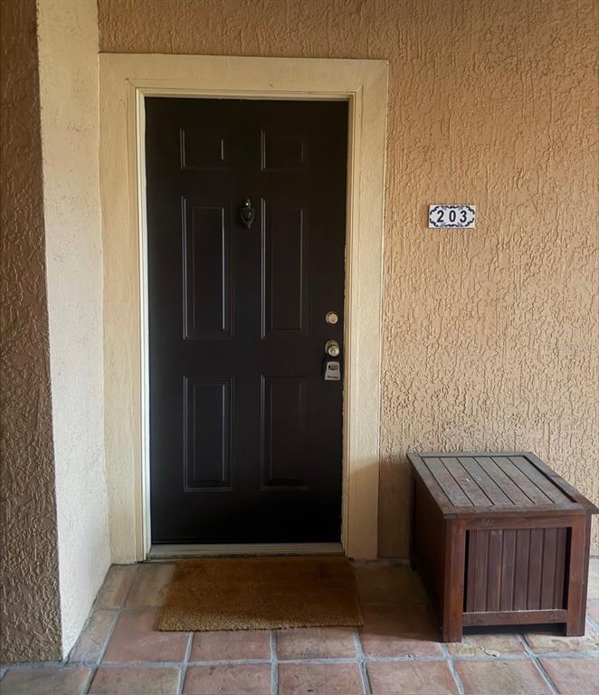 A dark brown front door with a door knocker and lockbox sits beside a wooden chest — 5572 METROWEST BLVD UNIT 203, ORLANDO, FL