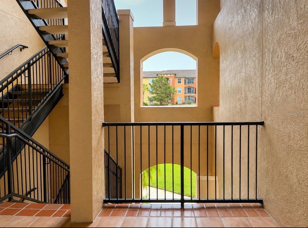 An outdoor stairwell with black metal railings overlooks a courtyard and a neighboring apartment building — 5572 METROWEST BLVD UNIT 203, ORLANDO, FL