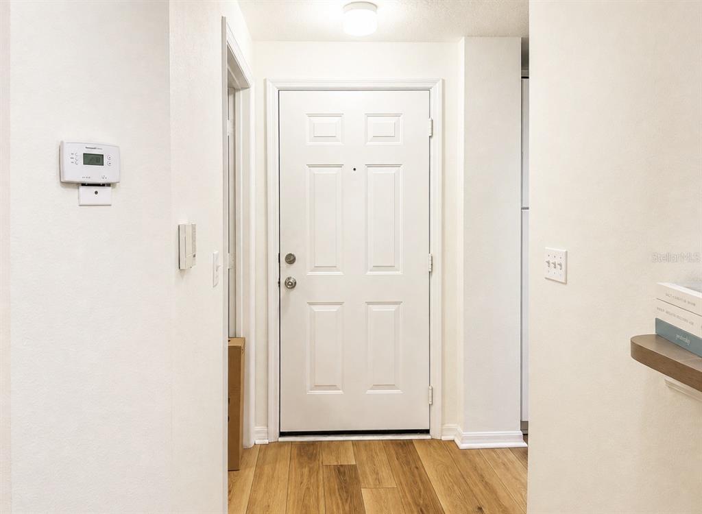 A white front door with wood-look flooring in a brightly lit residential entryway — 5572 METROWEST BLVD UNIT 203, ORLANDO, FL