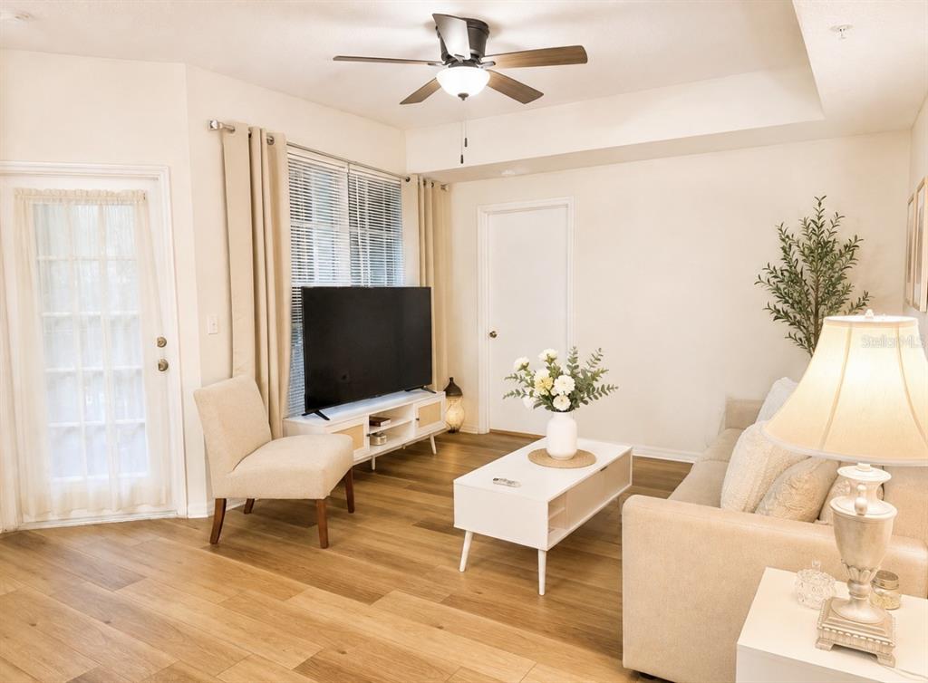 A living room features light wood flooring, a ceiling fan, a television, and neutral furniture — 5572 METROWEST BLVD UNIT 203, ORLANDO, FL