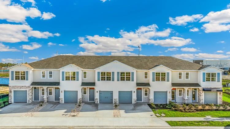 A multi-unit townhouse building features light-colored siding, stone accents, and attached garages under a blue sky — 10690 TIGER LILY DRIVE, VENICE, FL