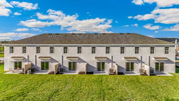 The rear exterior of a multi-unit townhouse building features sliding glass doors and small patios — 10690 TIGER LILY DRIVE, VENICE, FL