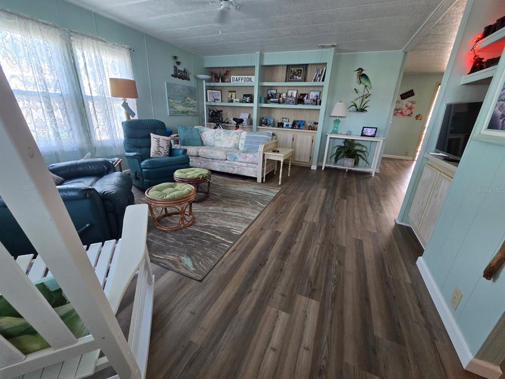 A living room features light blue walls, wood-look flooring, a floral sofa, and built-in shelving — 86 PARSON DRIVE, WINTER HAVEN, FL