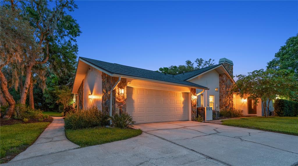 A single-story house with a stone facade, two-car garage, and a concrete driveway at dusk — 2423 FOXHEAD WAY, CLEARWATER, FL