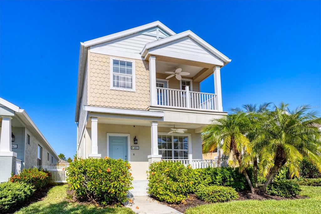 A two-story house with a front porch, balcony, and light-colored siding under a clear sky — 4811 WOODBROOK DRIVE, SARASOTA, FL