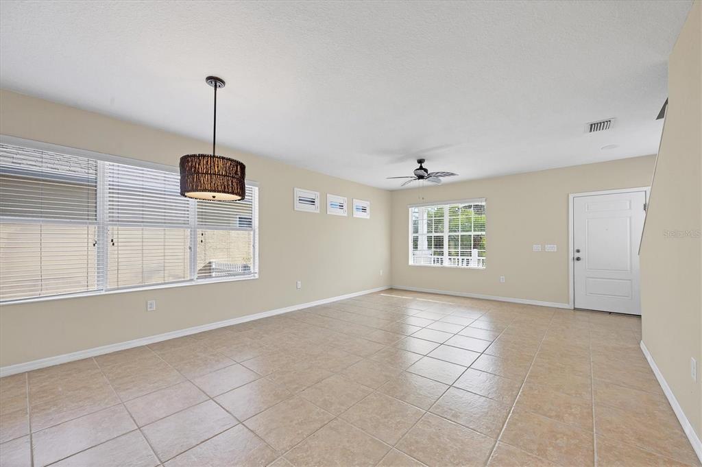 An empty living area features beige tile flooring, light-colored walls, a ceiling fan, and windows — 4811 WOODBROOK DRIVE, SARASOTA, FL