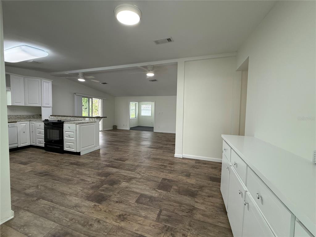 An open-concept kitchen and living area feature white cabinetry, dark countertops, and wood-look flooring — 8 ROBIN ROAD, WILDWOOD, FL