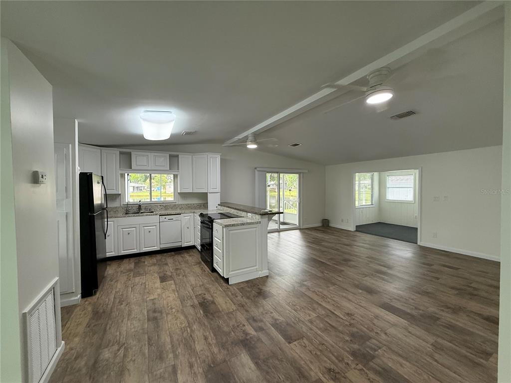 An open-concept kitchen and living area feature white cabinetry, dark appliances, and wood-look flooring — 8 ROBIN ROAD, WILDWOOD, FL