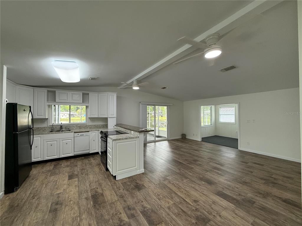 A kitchen with white cabinets and a black refrigerator opens into a living area — 8 ROBIN ROAD, WILDWOOD, FL