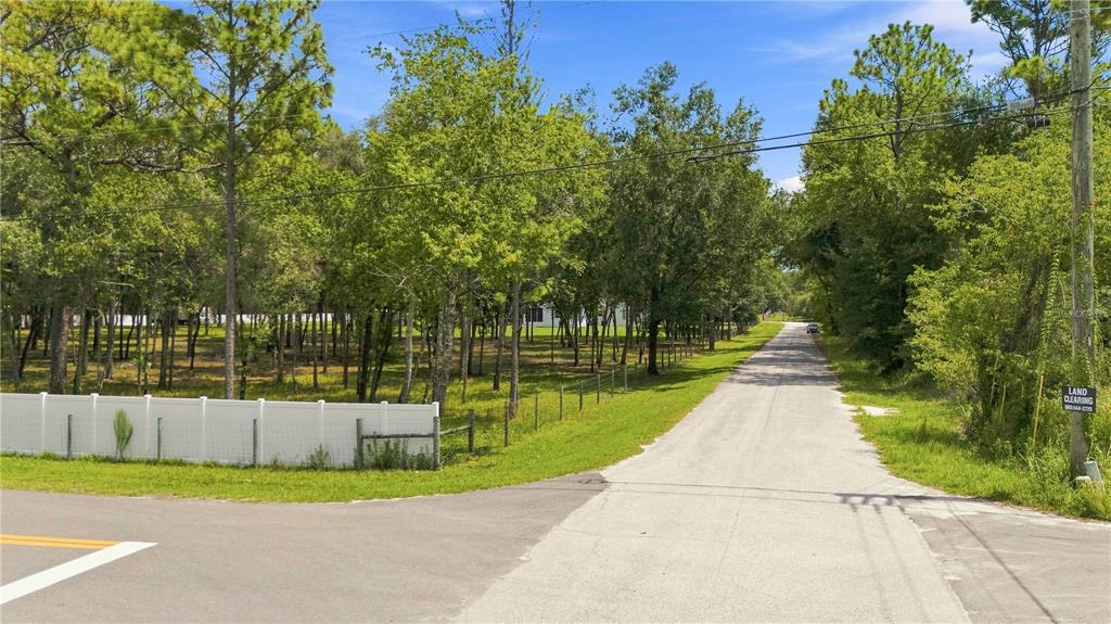 A paved road runs alongside a wooded lot enclosed by a white vinyl fence — 14313 HIGHGROVE ROAD, BROOKSVILLE, FL