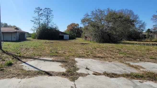 A vacant lot features a concrete driveway, scattered trees, and two small outbuildings in the background — 6012 LORRAINE ROAD, BRADENTON, FL