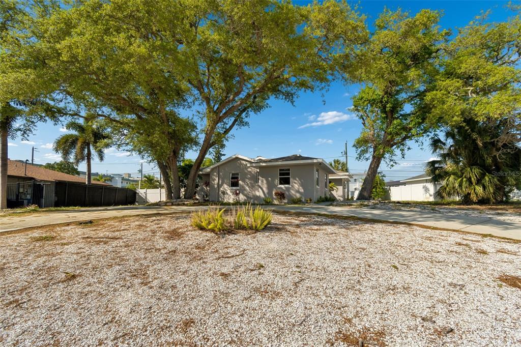 A light-colored single-story house sits behind a large gravel yard with mature shade trees — 125 HARBOR BLUFF DRIVE, LARGO, FL