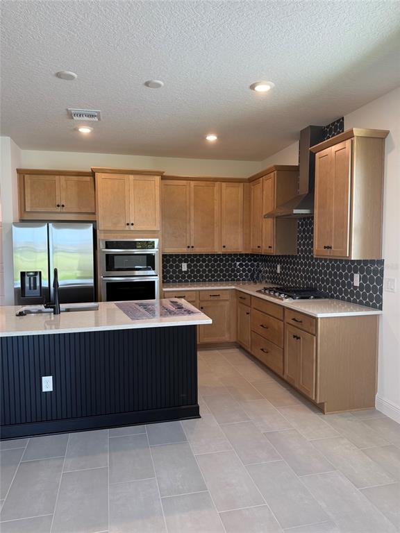 A kitchen features light wood cabinets, a black island, stainless steel appliances, and hexagon tile backsplash — 5123 BUTTONSAGE DRIVE, ST CLOUD, FL