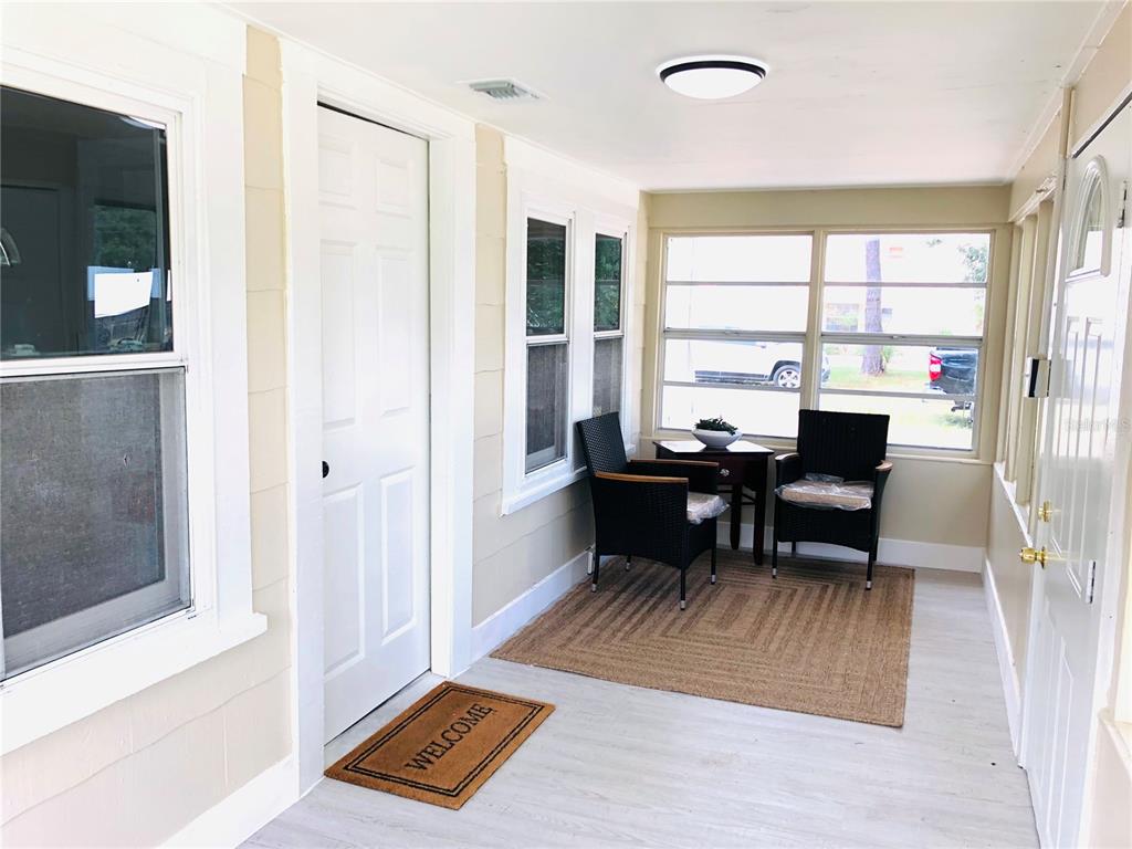 A sunroom features light-colored walls, a white door, two wicker chairs, and a welcome mat — 908 VINE AVENUE, CLEARWATER, FL