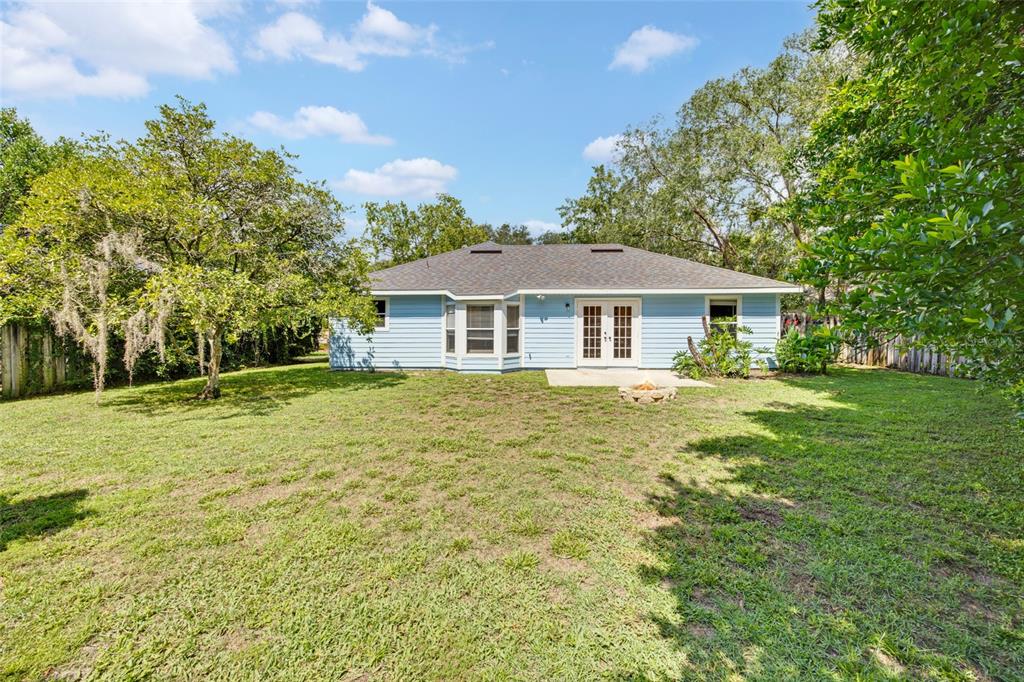 The rear exterior of a light blue house features a small patio and a grassy yard — 4341 NW 34TH TERRACE, GAINESVILLE, FL