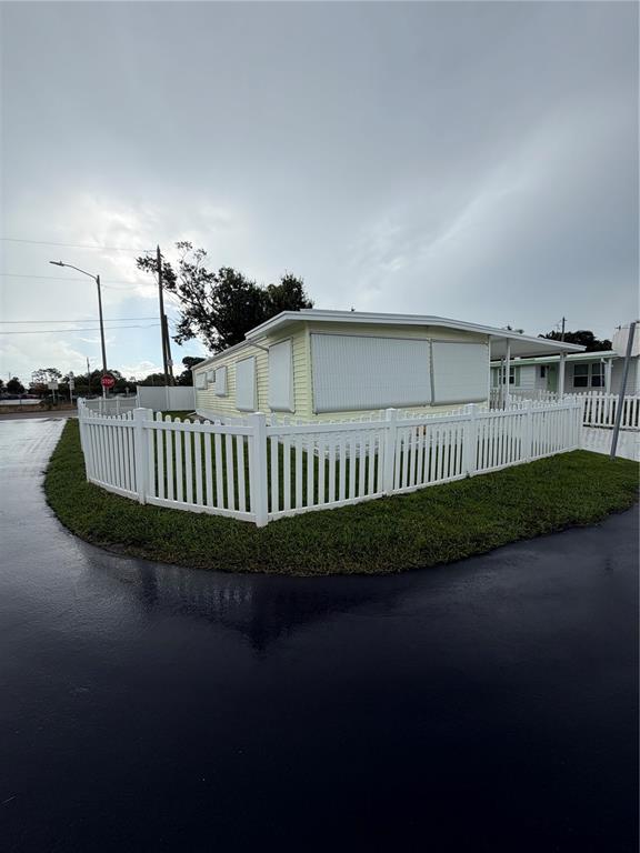 A yellow mobile home with white shutters and a white picket fence under a cloudy sky — 9900 ULMERTON ROAD UNIT 49, LARGO, FL