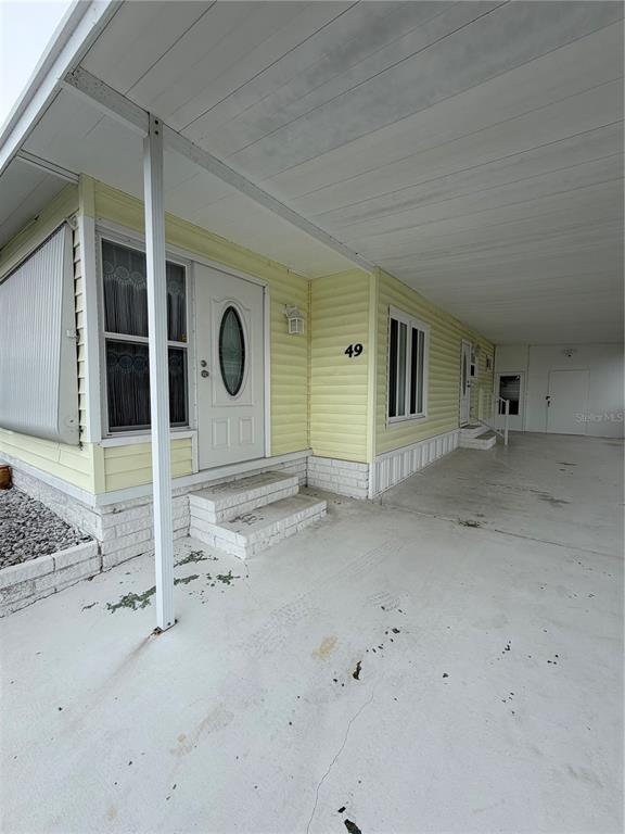 A yellow mobile home exterior features a white front door, a carport, and concrete steps — 9900 ULMERTON ROAD UNIT 49, LARGO, FL