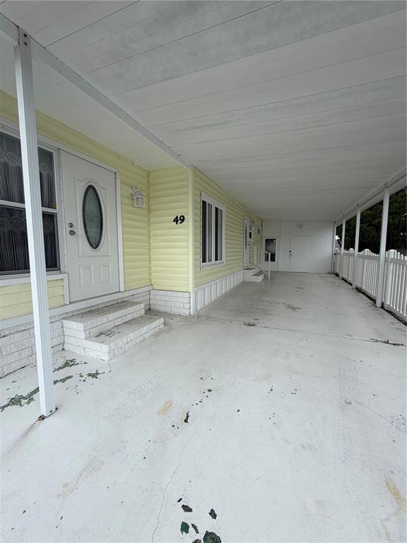 A yellow mobile home exterior features a white front door, concrete steps, and a carport — 9900 ULMERTON ROAD UNIT 49, LARGO, FL