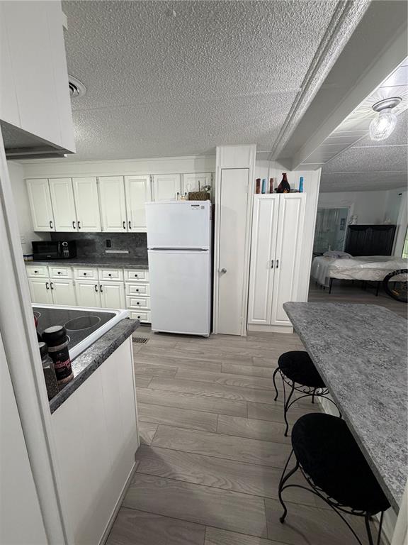 A kitchen features white cabinetry, a white refrigerator, grey countertops, and light wood-look flooring — 9900 ULMERTON ROAD UNIT 49, LARGO, FL