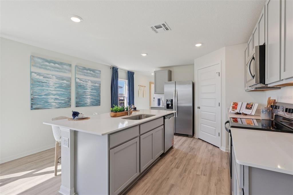 A modern kitchen features gray cabinets, a white quartz island with a sink, and stainless appliances — 1522 LAS PALMAS STREET, LAKELAND, FL