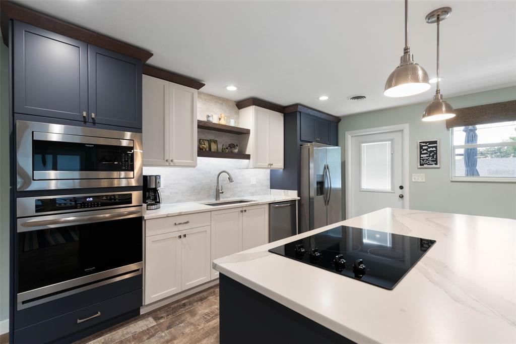 A modern kitchen features two-toned navy and white cabinetry, stainless steel appliances, and a central island — 76 BANYAN DRIVE, ORMOND BEACH, FL