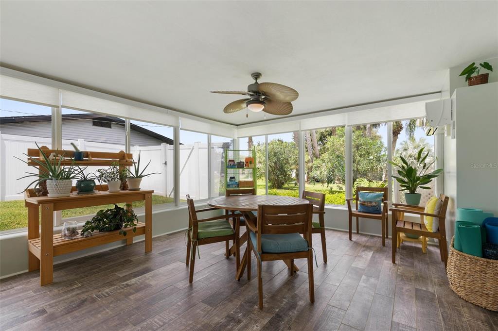 A sunroom features wood-look tile flooring, a dining set, a potting bench, and large windows — 76 BANYAN DRIVE, ORMOND BEACH, FL