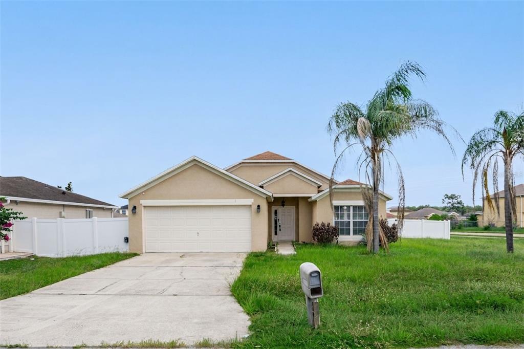 A single-story tan stucco house with a two-car garage and a palm tree in front — 1 CATALINA COURT, KISSIMMEE, FL