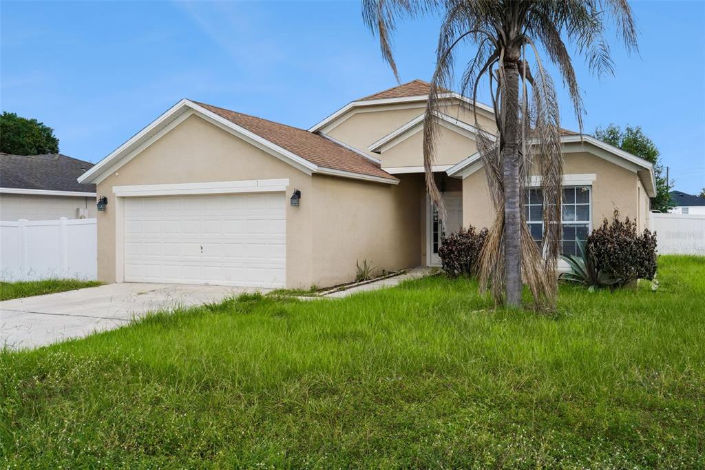 A single-story tan stucco house with a two-car garage and a palm tree in front — 1 CATALINA COURT, KISSIMMEE, FL