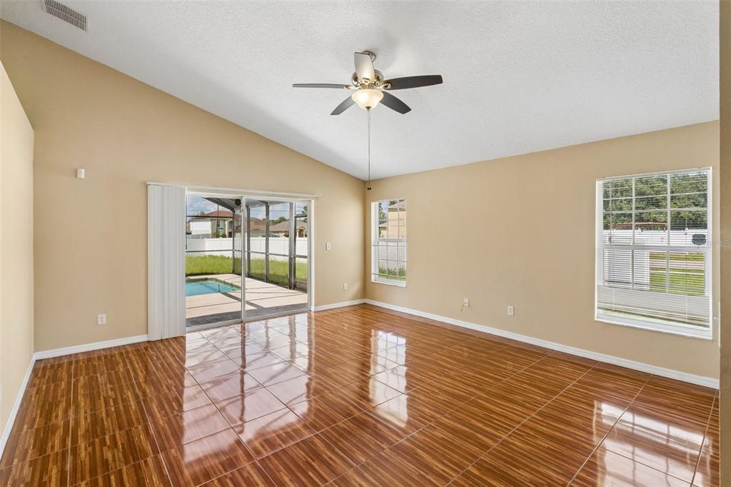 An empty living room features vaulted ceilings, glossy wood-look tile floors, and a sliding glass door — 1 CATALINA COURT, KISSIMMEE, FL