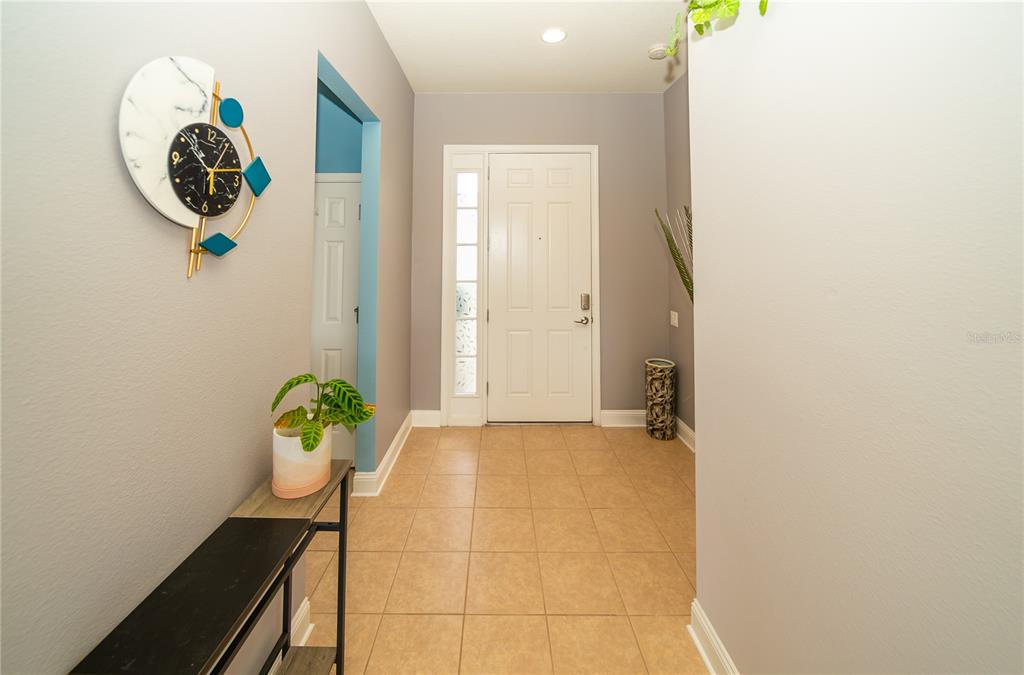 A tiled entryway features a white front door, a wall clock, and a console table — 5109 99TH AVENUE E, PARRISH, FL