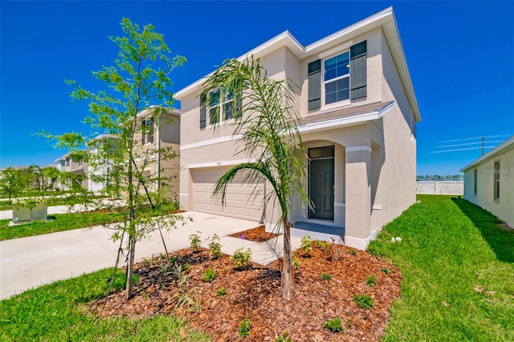 A two-story beige house with a two-car garage and a small palm tree in front — 9138 FORGE BREEZE LOOP, WESLEY CHAPEL, FL