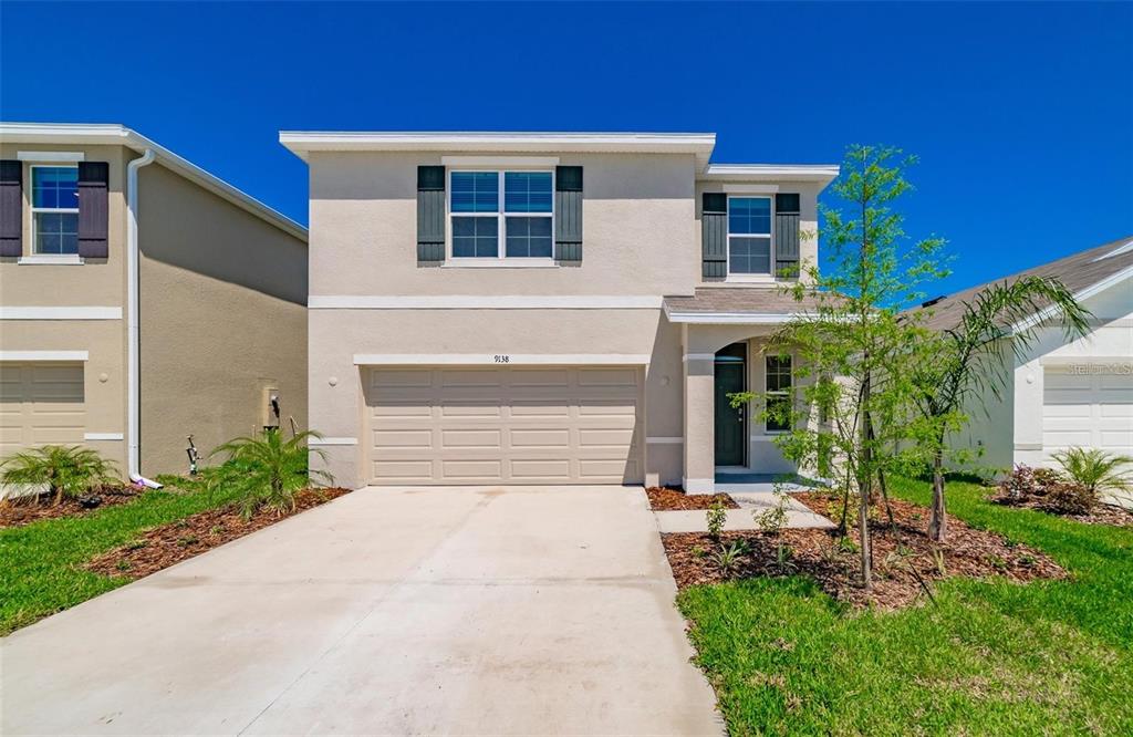 A two-story suburban house with a beige stucco exterior, a two-car garage, and landscaping — 9138 FORGE BREEZE LOOP, WESLEY CHAPEL, FL