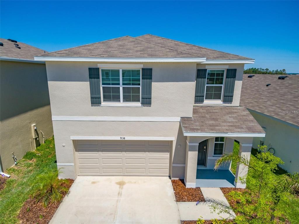 A two-story suburban house with a beige stucco exterior, a garage, and a front porch — 9138 FORGE BREEZE LOOP, WESLEY CHAPEL, FL