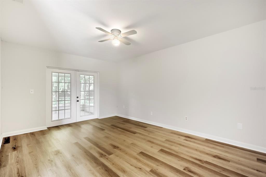 An empty room with light wood-look flooring, white walls, a ceiling fan, and French doors — 1418 OAK VALLEY DRIVE, SEFFNER, FL