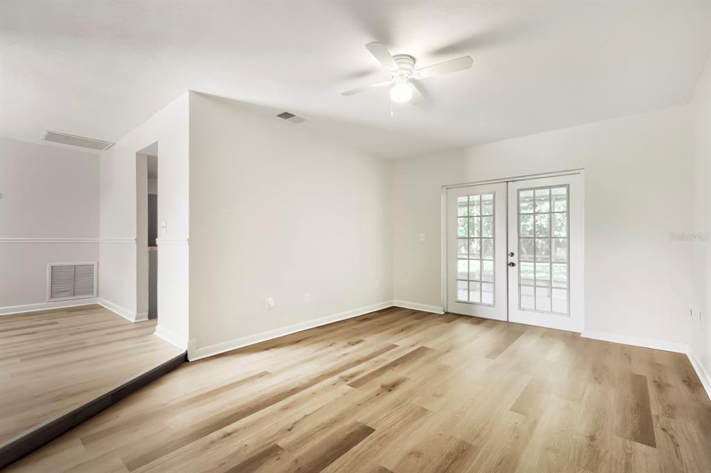 An empty room with light wood-look flooring, white walls, a ceiling fan, and glass French doors — 1418 OAK VALLEY DRIVE, SEFFNER, FL