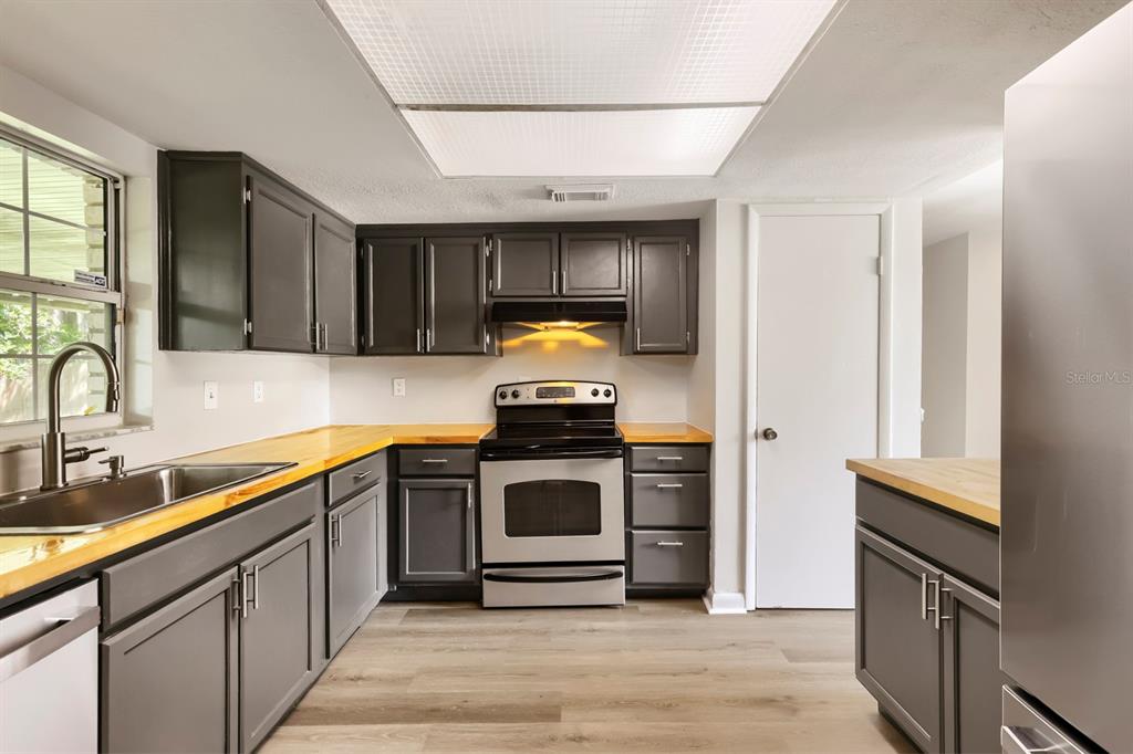 A kitchen features dark gray cabinets, light wood countertops, stainless steel appliances, and wood-look flooring — 1418 OAK VALLEY DRIVE, SEFFNER, FL